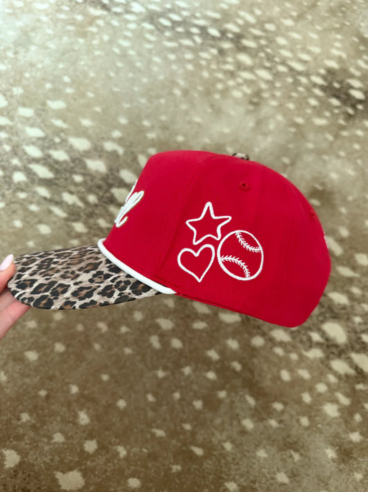 Red cap with leopard print brim held against a spotted animal background