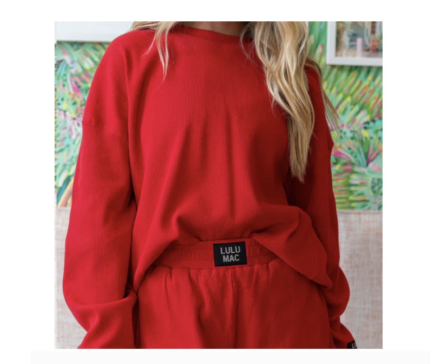 Red outfit with a visible brand label against a colorful abstract painting background