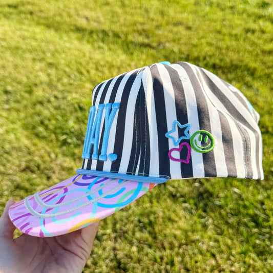 Striped cap with colorful text and designs held in front of a grassy background