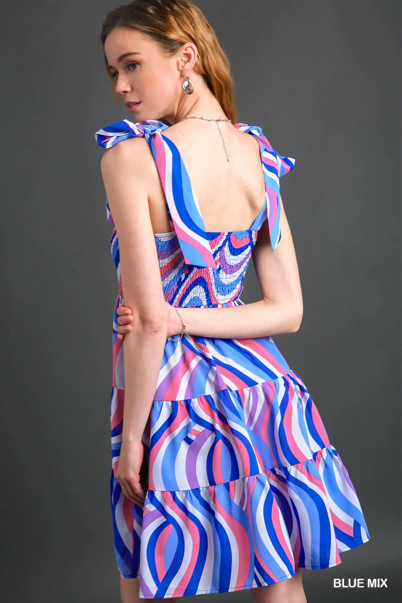 Woman wearing a colorful dress with a blue, pink, and purple pattern on a gray background