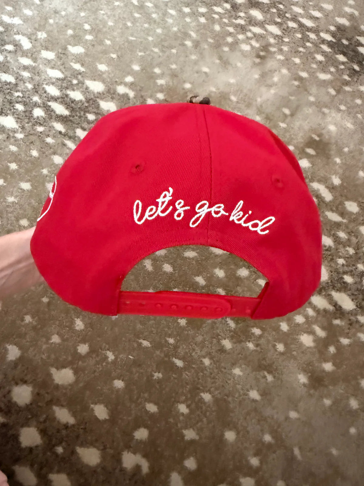 Red cap with 'let's go kid' text on a textured surface