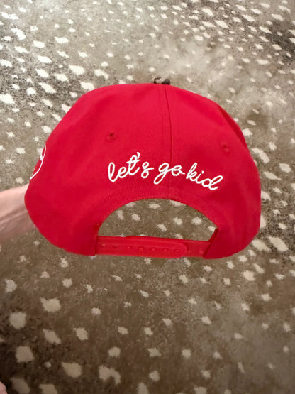 Red cap with 'let's go kid' text on a textured surface