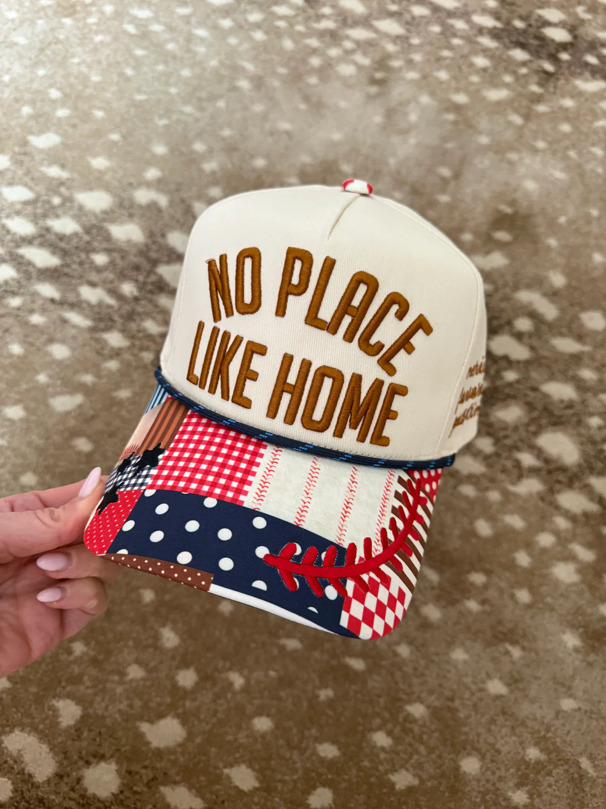Cap with 'No Place Like Home' text held by a hand on a patterned surface