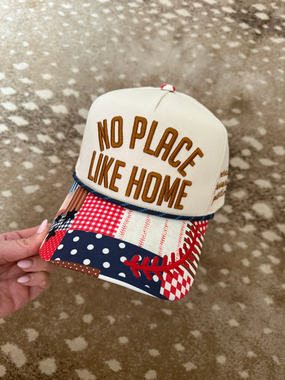 Cap with 'No Place Like Home' text held by a hand on a patterned surface