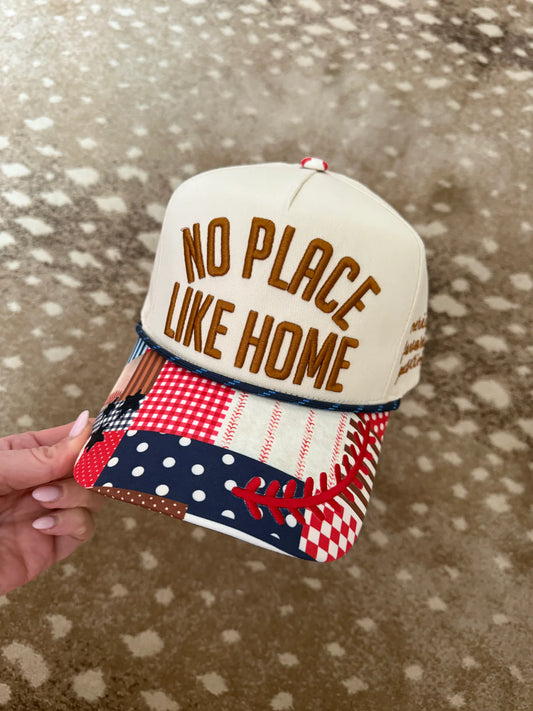 Cap with 'No Place Like Home' text held by a hand on a patterned surface