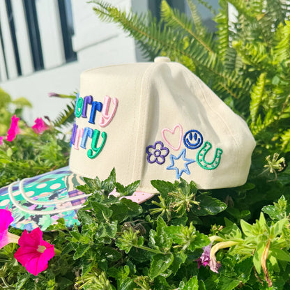 Beige cap with colorful embroidered text and designs on a green plant background