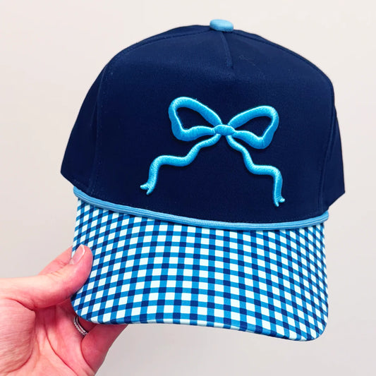 Navy blue cap with a blue bow and checkered visor held by a hand against a light gray background