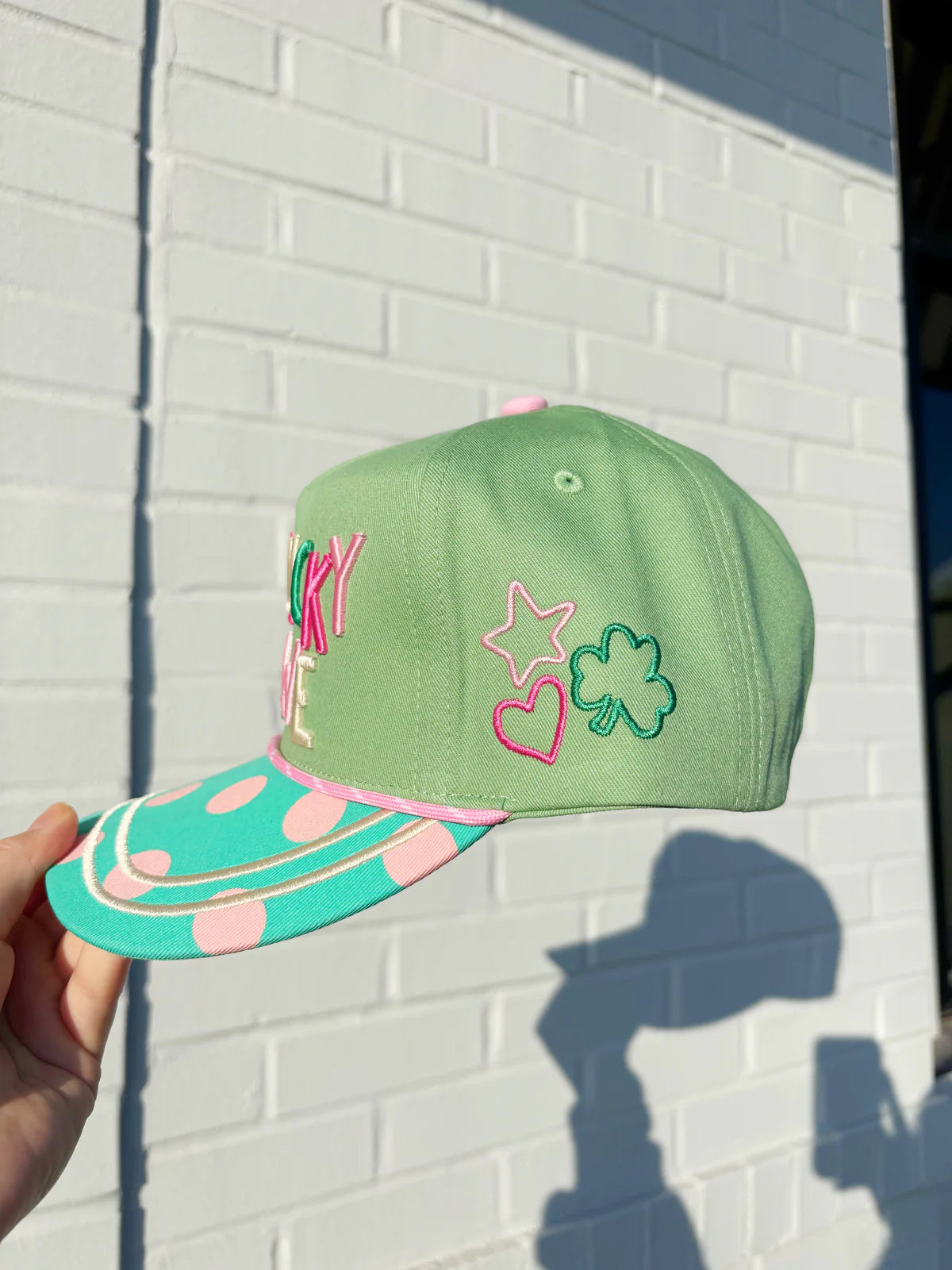 Green cap with colorful designs held against a white brick wall
