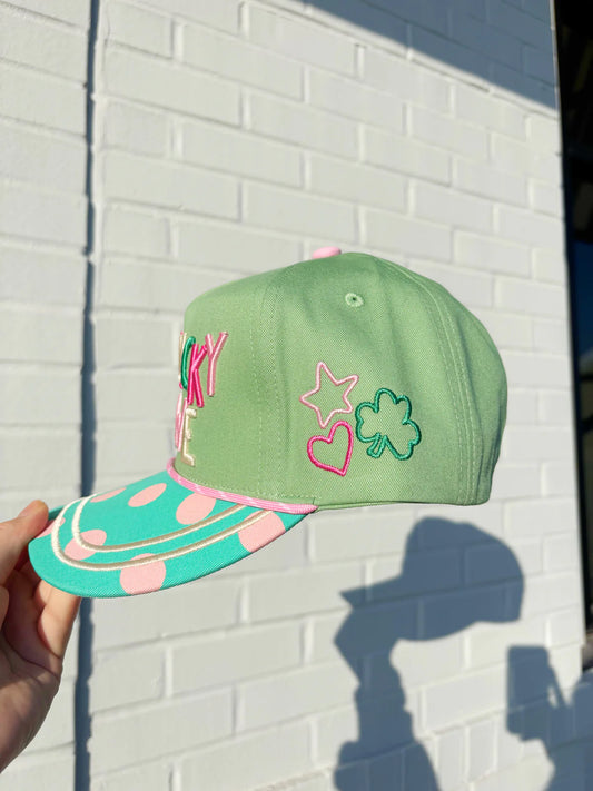 Green cap with colorful designs held against a white brick wall