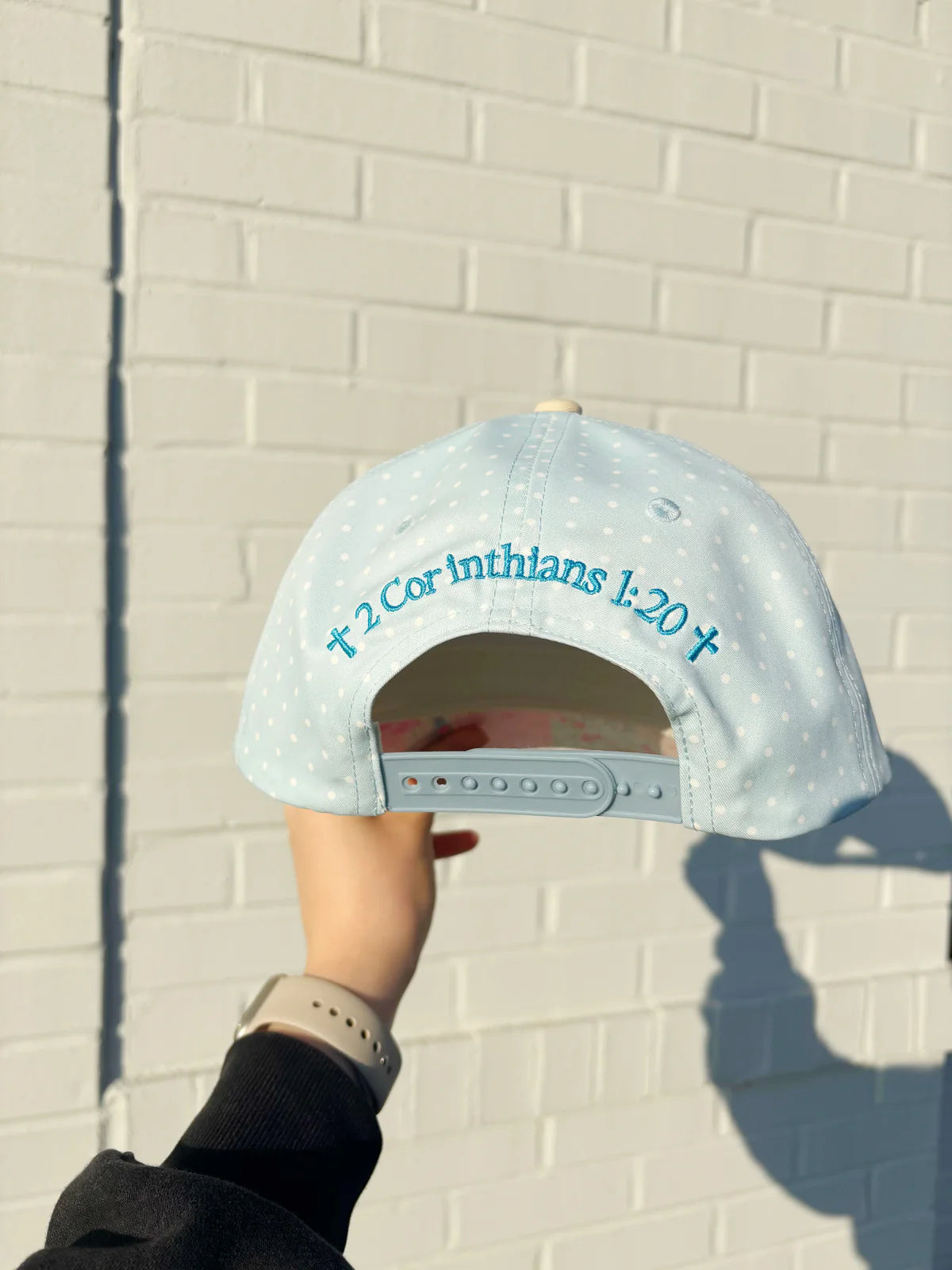 Light blue cap with text held against a white brick wall