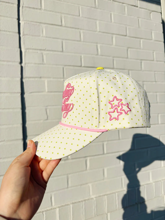White cap with pink accents held against a light brick wall