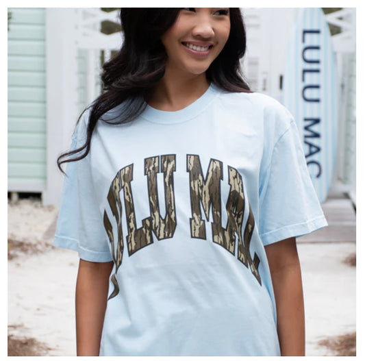 Woman wearing a light blue t-shirt with 'LULU MAC' printed on it, standing outdoors.
