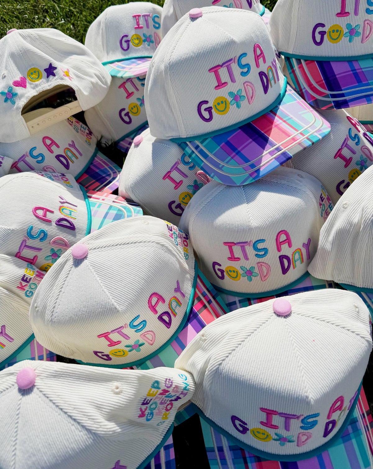 Stack of white caps with 'It's a Good Day' text in various colors on a colorful background