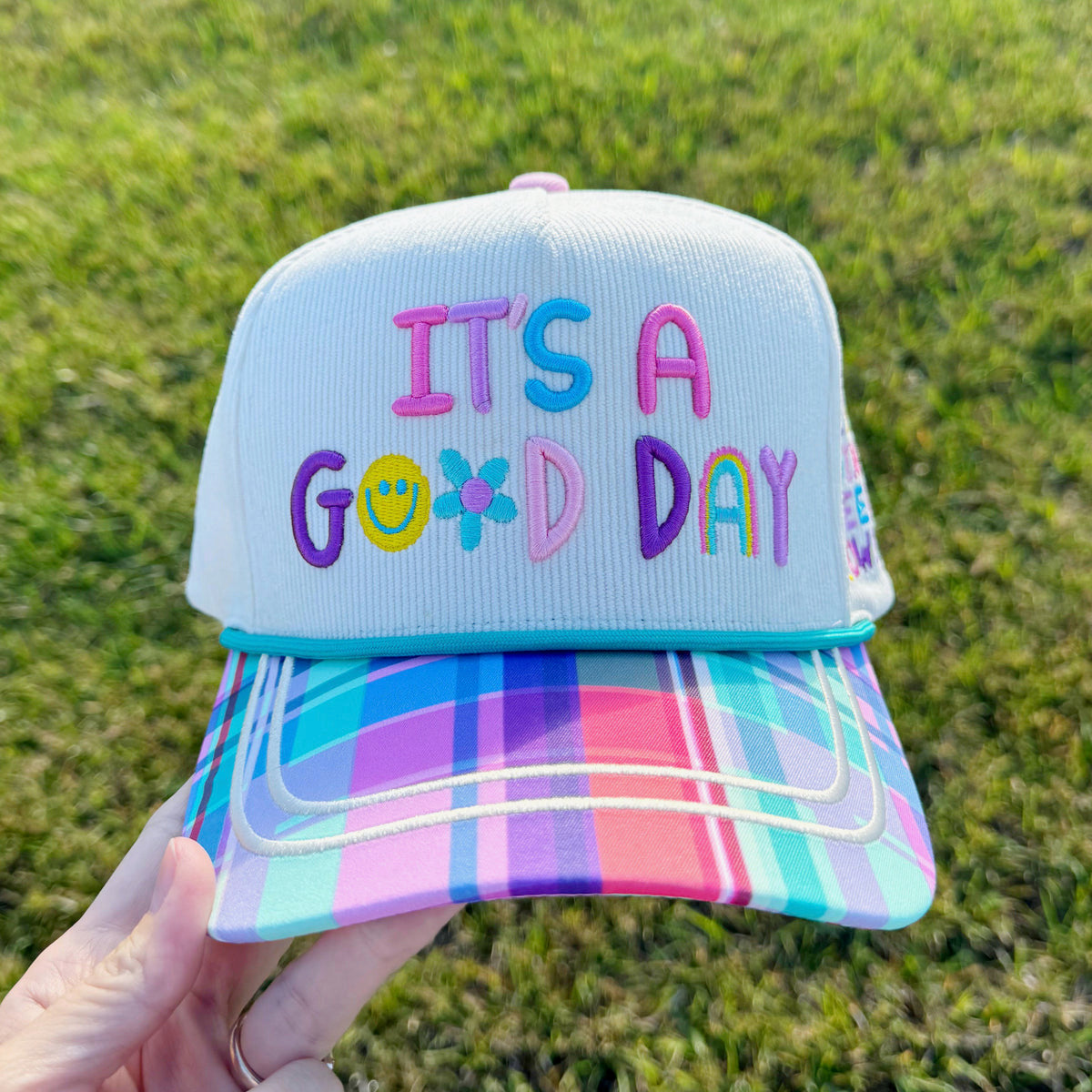 Colorful cap with 'It's a Good Day' text held against a grassy background