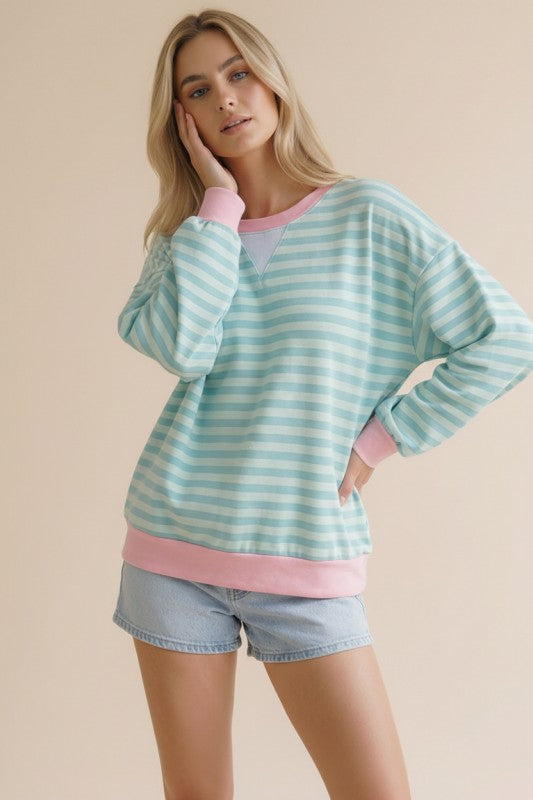 Woman wearing a light blue and pink striped sweater with denim shorts on a beige background
