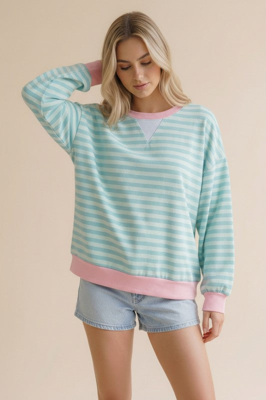 Woman wearing a light blue and pink striped sweater with denim shorts on a beige background