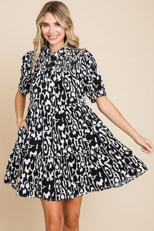 A woman wearing a black and white animal patterned smock dress with a collared neck and short sleeves.