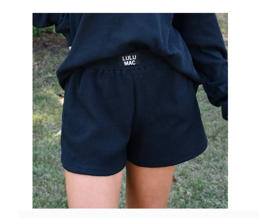 Person wearing navy shorts with 'LULU MAC' branding, standing on grass.