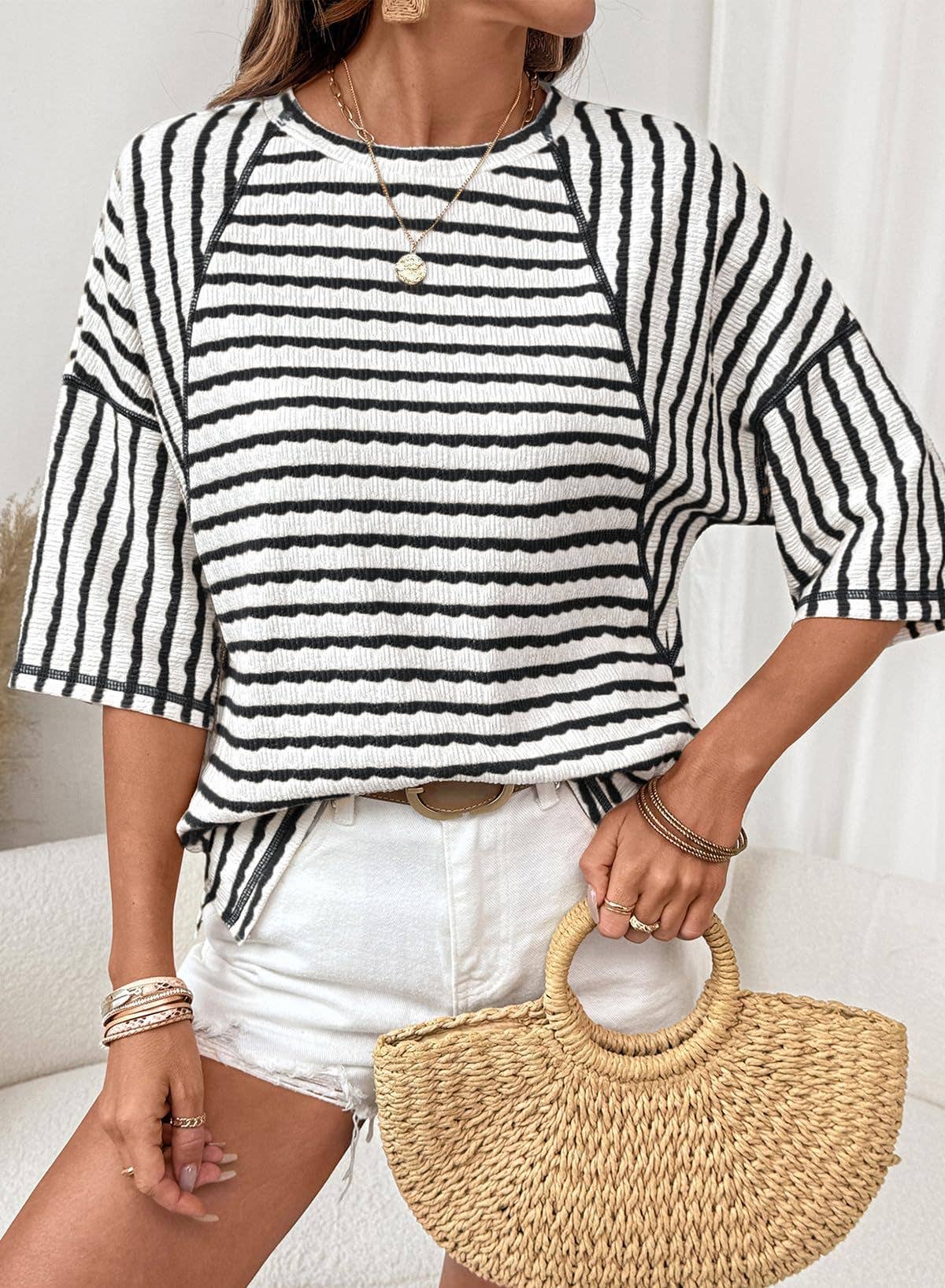 Person wearing a black and white striped shirt with white shorts, holding a straw bag.